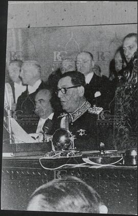 [Perón sentado dando un discurso con micrófono]